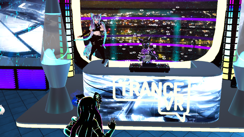 A virtual trance DJ set in VRChat, shown inside a futuristic neon venue. A purple-and-black avatar performs behind a glowing DJ booth marked “TRANCE VR,” while a blue-haired avatar dances beside the booth and another avatar watches from the foreground.